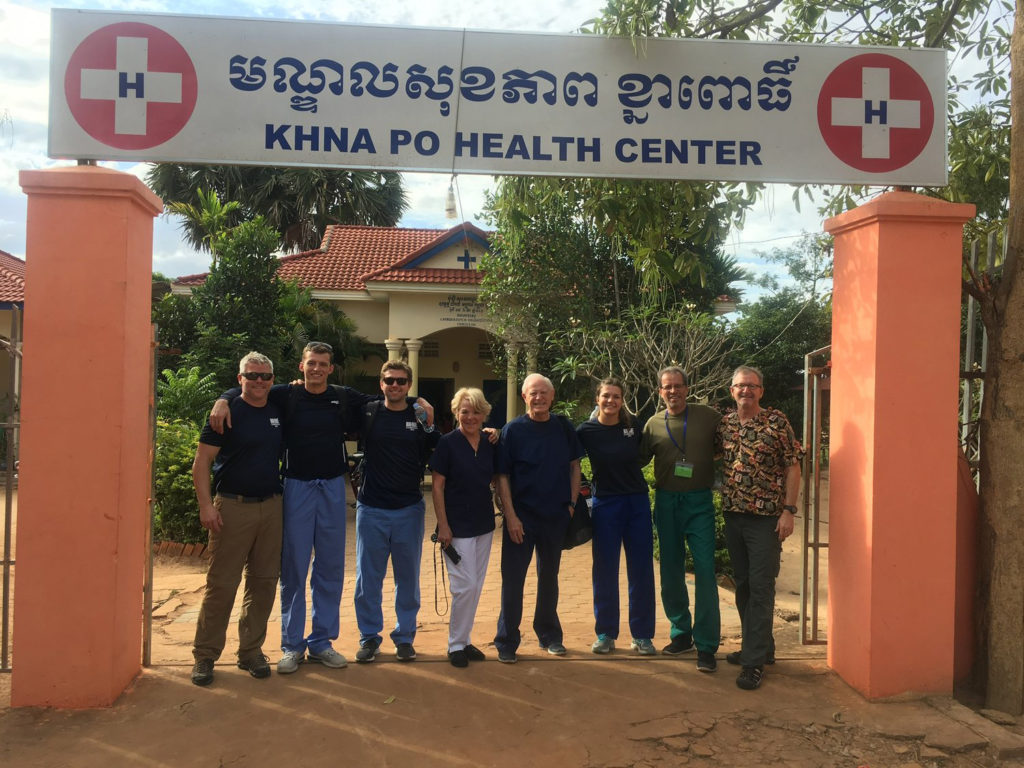 Eight people standing side by side under the KHNA PO HEALTH CENTER arch